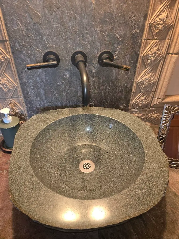 Wall-mounted faucet over a stone vessel sink in an older home